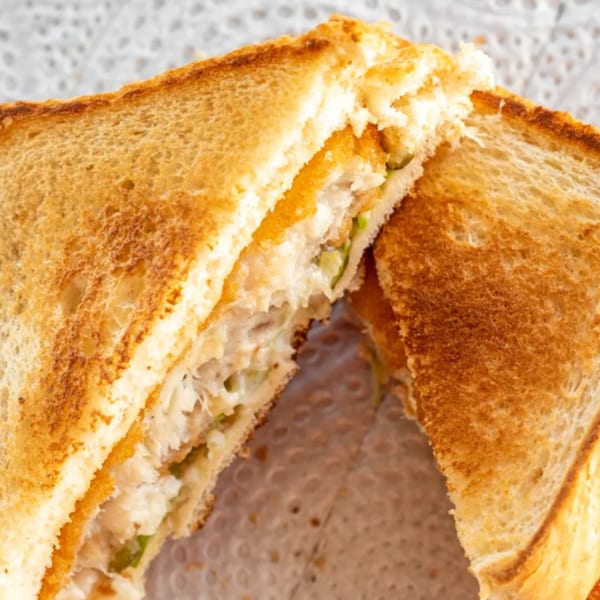 Close-up of a toasted sandwich cut in half, revealing a creamy filling with green specks.