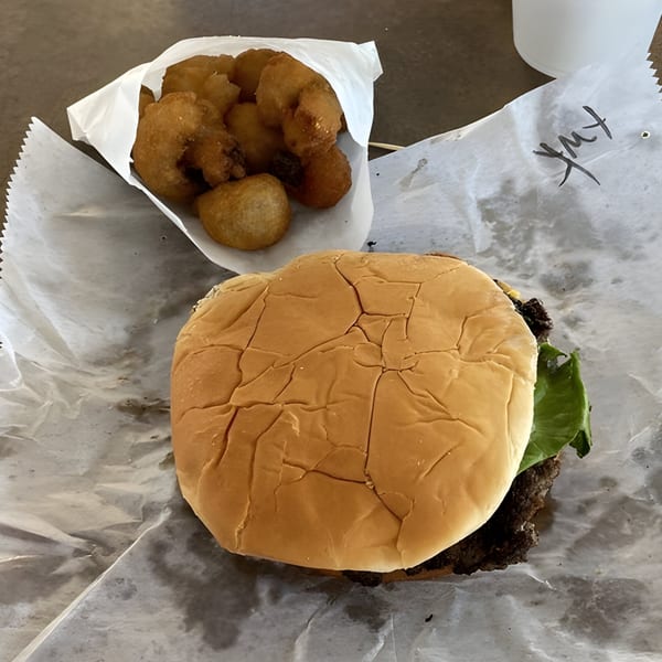 R-B Drive In burger with lettuce and a side of golden-brown fried hushpuppies on wax paper.