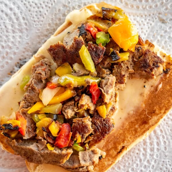 Close-up of a cheesesteak sandwich with grilled meat, colorful bell peppers, and melted cheese.