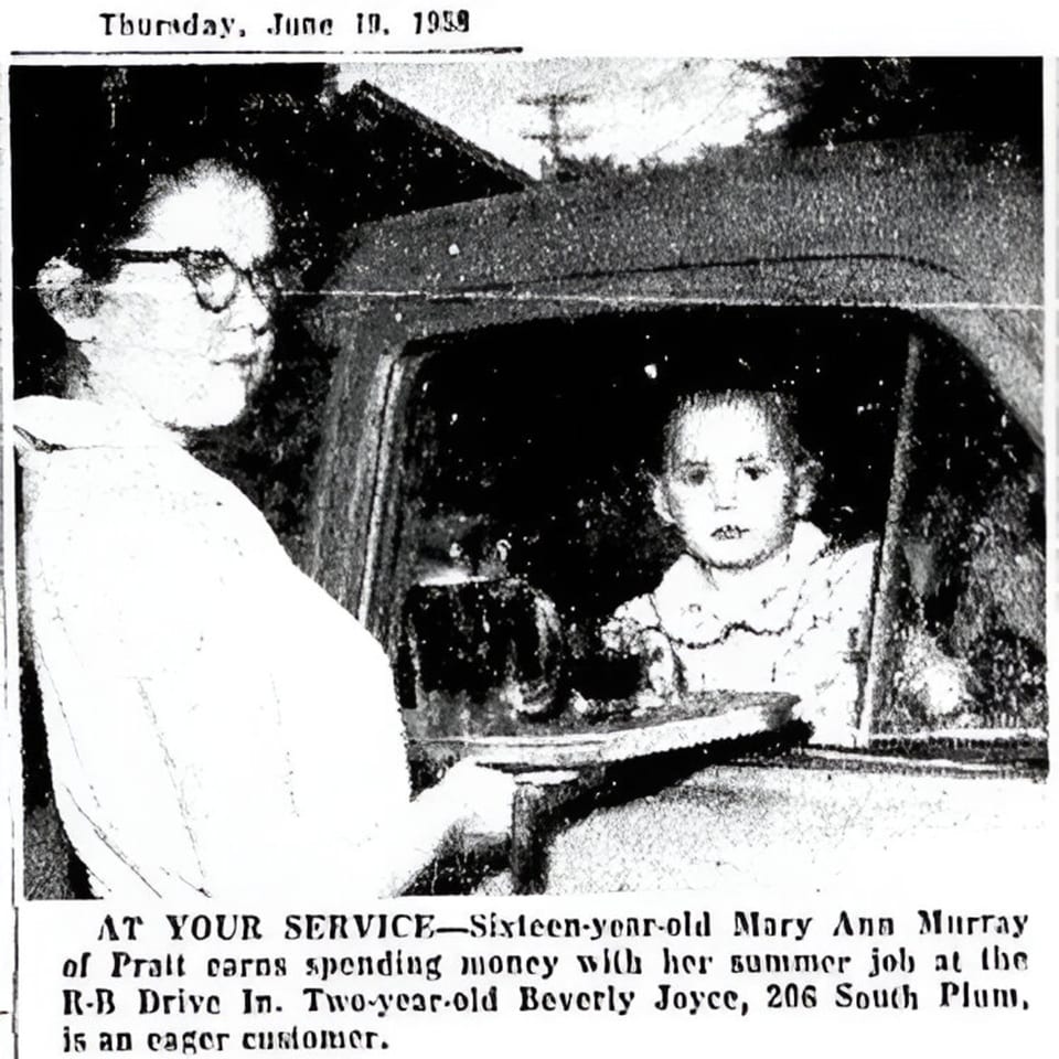 A carhop serving a burger to a young child in a car at the R-B Drive In.