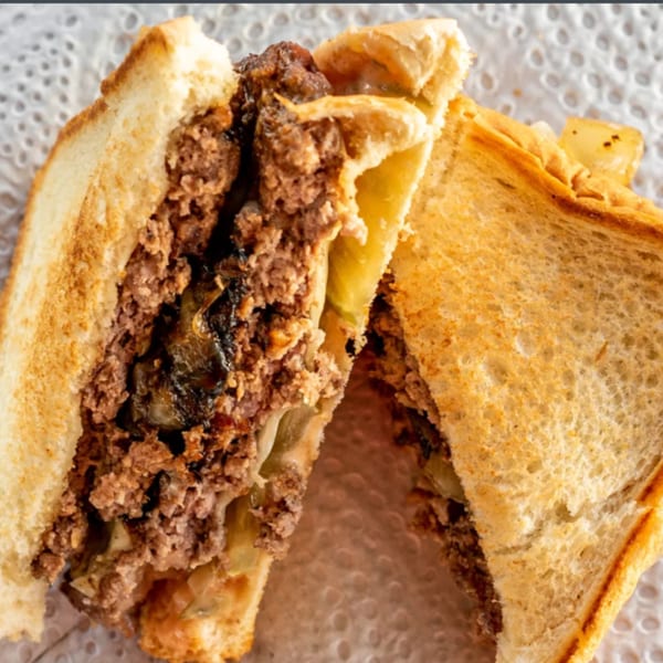 Close-up of an R-B Drive In patty melt, cut in half, revealing ground beef, onions, and melted cheese.
