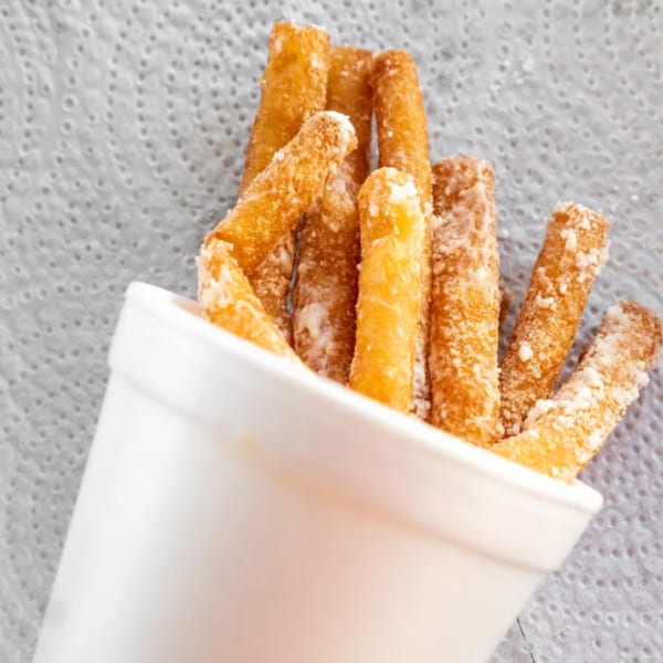 Close-up of golden-brown, crispy french fries, lightly dusted with salt, in a white cup.